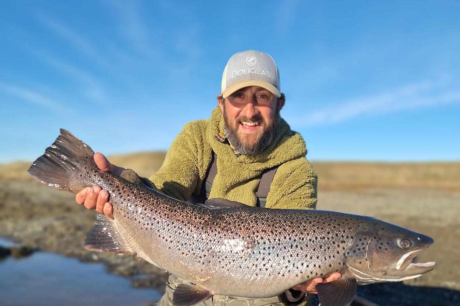 Pêcheur avec une grosse truite de mer sous le ciel de Terre de Feu